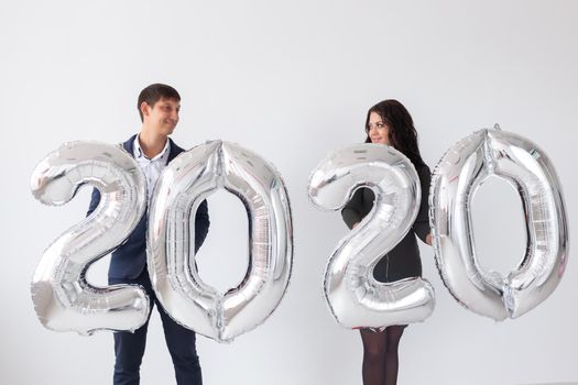 New year, celebration and holidays concept - love couple with sign 2020 made of silver balloons for new year on white background.