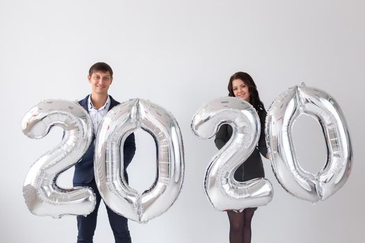 New year, celebration and holidays concept - love couple with sign 2020 made of silver balloons for new year on white background.