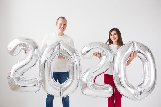 New year, celebration and holidays concept - love couple with sign 2020 made of silver balloons for new year on white background.