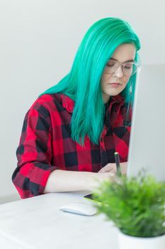 Designer, illustrator, artist and people concept - portrait of contemporary young woman with green hair using laptop and graphic tablet while working.