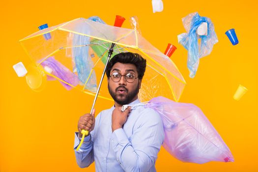 Environmental pollution, plastic recycling problem and waste disposal concept - surprised indian man holding garbage bag on yellow background