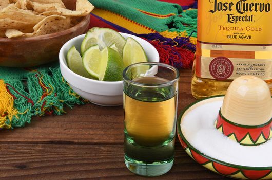 IRVINE, CALIFORNIA - 12 JAN 2017: Jose Cuervo Tequila Gold bottle with shot glass and limes, salt, chips and Mexican blanket. 