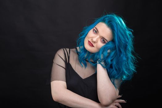 People and fashion concept - Young and attractive woman with black lipstick and blue hair posing over black background.