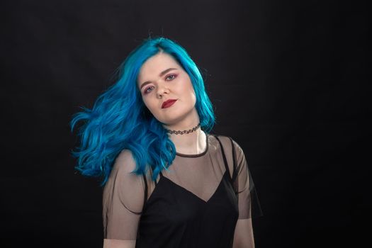 People and fashion concept - Young and attractive woman with black lipstick and blue hair posing over black background.