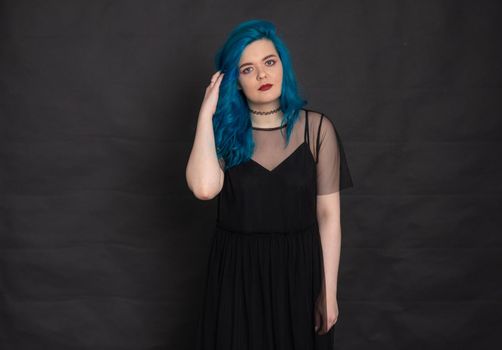 People and fashion concept - Woman dressed in black dress and blue hair posing over black background.