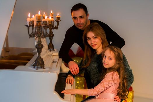 Happy Family Posing in Luxurious Interior near Piano Decorated with Burning Candles in Candlestick, Portrait of Parents and Charming Girl, Father Gently Looking at His Adorable Daughter