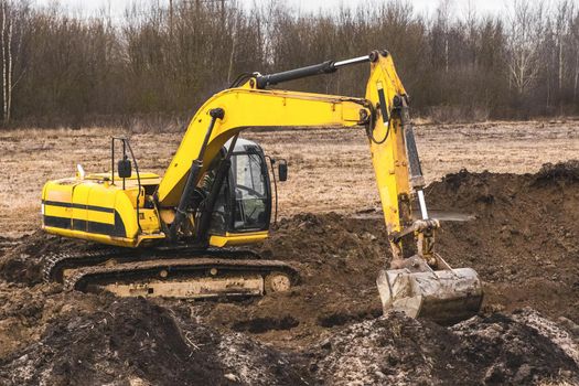 Construction worker on an crawler excavator equipment digs a trench in an industrial area. Excavation work with land and soil.