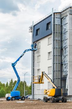 Belarus, Minsk - May 28, 2020: A worker on a lifting platform paints the facade of a new modern urban building under construction at a construction site.