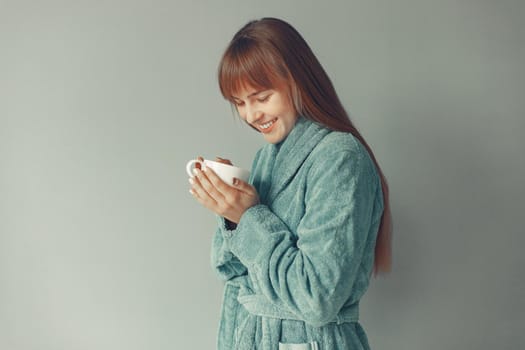 Girl in a studio. Lady in a blue bathrobe. Woman drinking a coffee