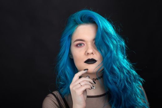 People and fashion concept - Young and attractive woman with black lipstick and blue hair posing over black background.