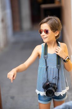 Little girl making photo with DSLR camera on city street. Small female traveling in urban background.
