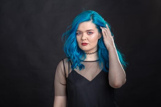 People and fashion concept - Young and attractive woman with black lipstick and blue hair posing over black background.