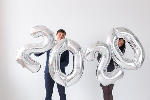 New year, celebration and holidays concept - love couple with sign 2020 made of silver balloons for new year on white background.