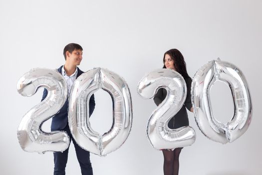 New year, celebration and holidays concept - love couple with sign 2020 made of silver balloons for new year on white background.