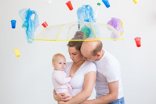 Plastic recycling problem, ecology and environmental disaster concept - family hiding from garbage under an umbrella on white background.