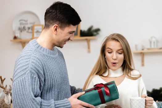 Sweet young couple opening Christmas gifts in the living room at home