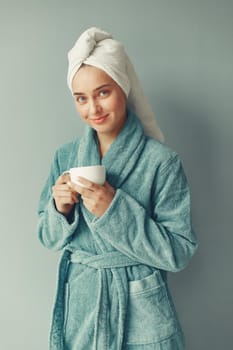 Girl in a studio. Lady in a blue bathrobe. Woman drinking a coffee