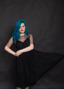 People and fashion concept - Woman dressed in black dress and blue hair posing over black background.