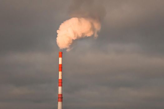 Environmental pollution problems and ecology concept. Smoke at sunset sky comes from a chimney of an industrial enterprise or thermal power plant and carbon dioxide is released into the atmosphere.