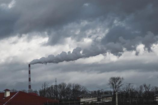 Environmental pollution, environmental problem, smoke from the chimney of a plant or thermal power plant against the dark grey sky.