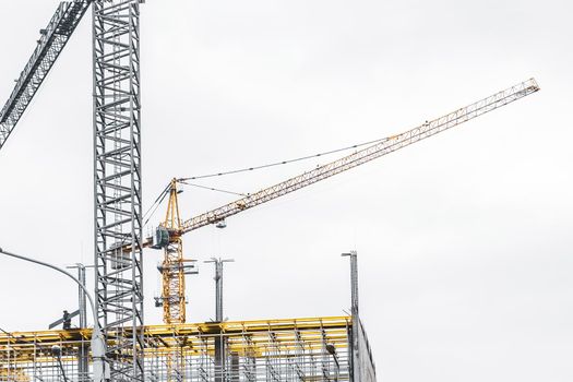 Tower crane against the gray sky builds a new city building or house on a construction site.