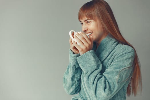 Girl in a studio. Lady in a blue bathrobe. Woman drinking a coffee