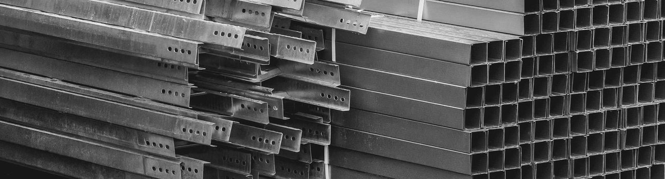 A pile of metal plates and square industrial pipes. Building materials at the construction site.