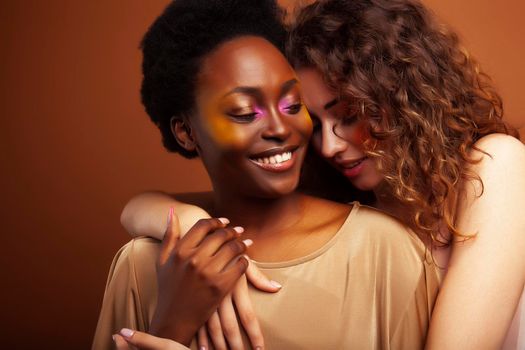 two pretty girls african and caucasian blond posing cheerful together on brown background, ethnicity diverse lifestyle people concept close up