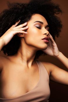 pretty young african american woman with curly hair posing cheerful gesturing on brown background, lifestyle people concept closeup