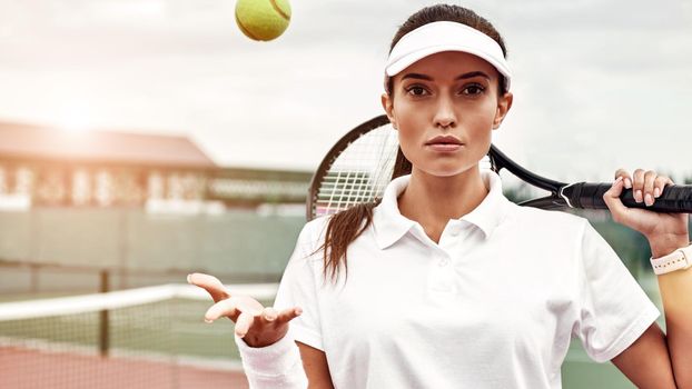 Beautiful woman in white polo with the racket and the ball standing on the tennis court. Horizontal shot