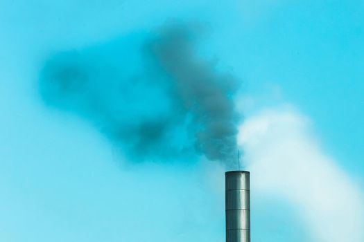 Environmental problem, environmental pollution, smoke from the pipe of an industrial plant or thermal power plant against a blue sky.