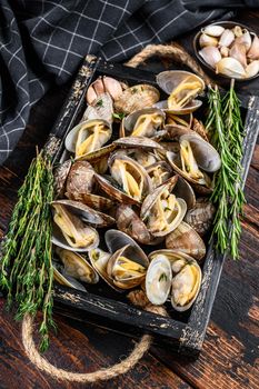 Clams vongole in a wooden tray with herbs. Dark wooden background. Top view.