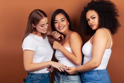 young pretty asian, caucasian, afro woman posing cheerful together on brown background, lifestyle diverse nationality people concept closeup