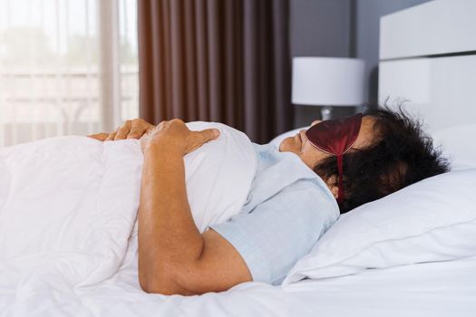 senior woman with eye mask sleeping on a bed in bedroom