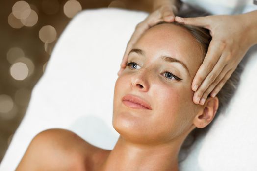 Young blond woman receiving a head massage in a spa center with blue eyes. Female patient is receiving treatment by professional therapist.