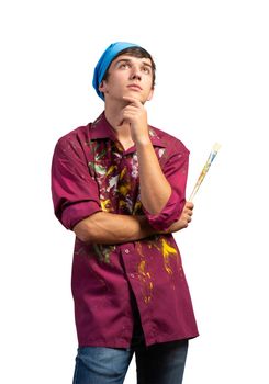 Young male painter artist holding paintbrush. Portrait of pensive painter in dirty shirt and bandana standing on white background. Creative hobby and artistic occupation. Art school courses concept.