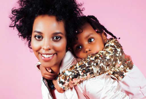 young pretty african-american mother with little cute daughter hugging, happy smiling on pink background, lifestyle modern people concept close up