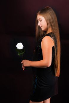 A teenage girl with a flower in her hand. Shooting in the studio on a black background.
