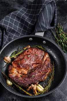 Roasted rib eye steak, ribeye beef meat in a pan. Black background. Top view.