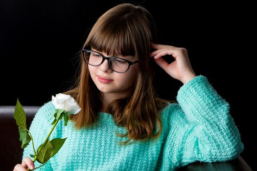 A teenage girl with a flower in her hand. Shooting in the studio on a black background.