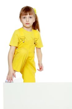 Girl with a short bangs on her head and bright yellow overalls.She put her foot on the white advertising banner.