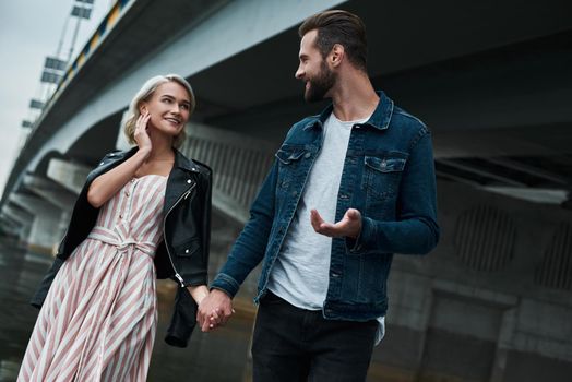 Romantic date outdoors. Young couple walking on the city street holding hands talking smiling joyful