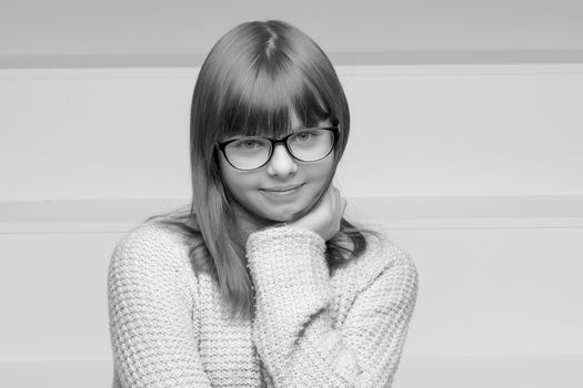 Beautiful schoolgirl girl in glasses sits on a white staircase. The concept of happy people, childhood.Black and white, monochrome photo.