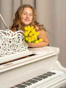 A school girl with a bouquet of flowers near a white grand piano.