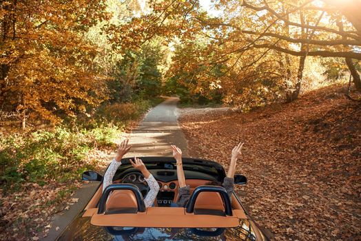 Female friends driving cabriolet with the hands up and having fun on the vacation