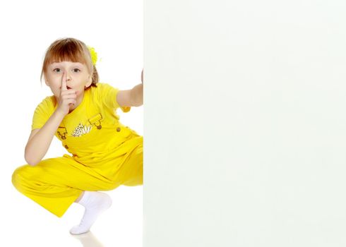 Girl with a short bangs on her head and bright yellow overalls.She crouched down on the white advertising banner.