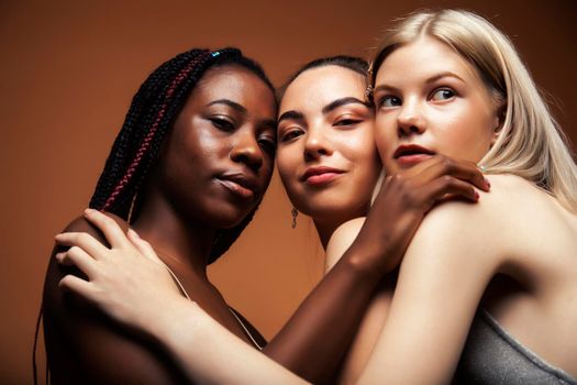 young pretty asian, caucasian, afro woman posing cheerful together on brown background, lifestyle diverse nationality people concept close up