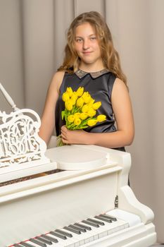 A school girl with a bouquet of flowers near a white grand piano.