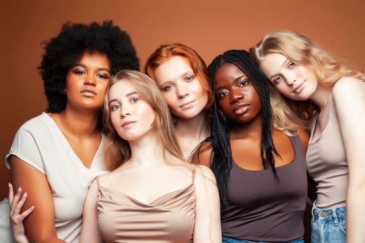 young pretty african and caucasian women posing cheerful together on brown background, lifestyle diverse nationality people concept closeup