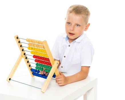 A cute little boy at school at a table studying mathematics. He uses abacus to solve mathematical problems. The concept of teaching a child in the family or at school.Isolated on white background.